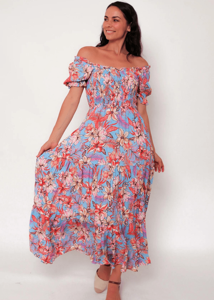Women's off or on the shoulder maxi dress with flounce sleeves, combining a vivid floral print in pinks, oranges, and whites on a light blue base. It features a fitted bodice, a gently gathered waist, and a flowing tiered skirt.