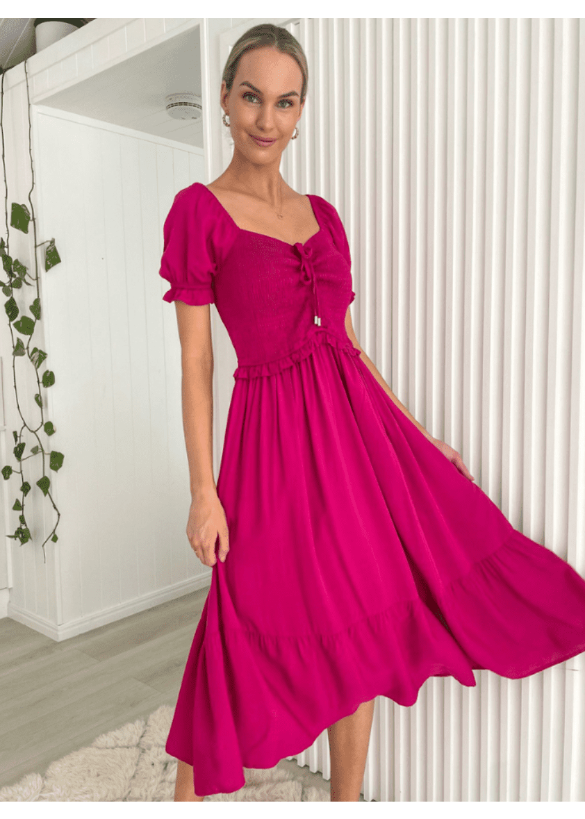 Vibrant fuchsia midi dress with puff sleeves and a subtle sweetheart neckline featuring a front tie detail. The dress has a cinched waist and a flowing skirt that reaches mid-calf, creating an elegant silhouette.